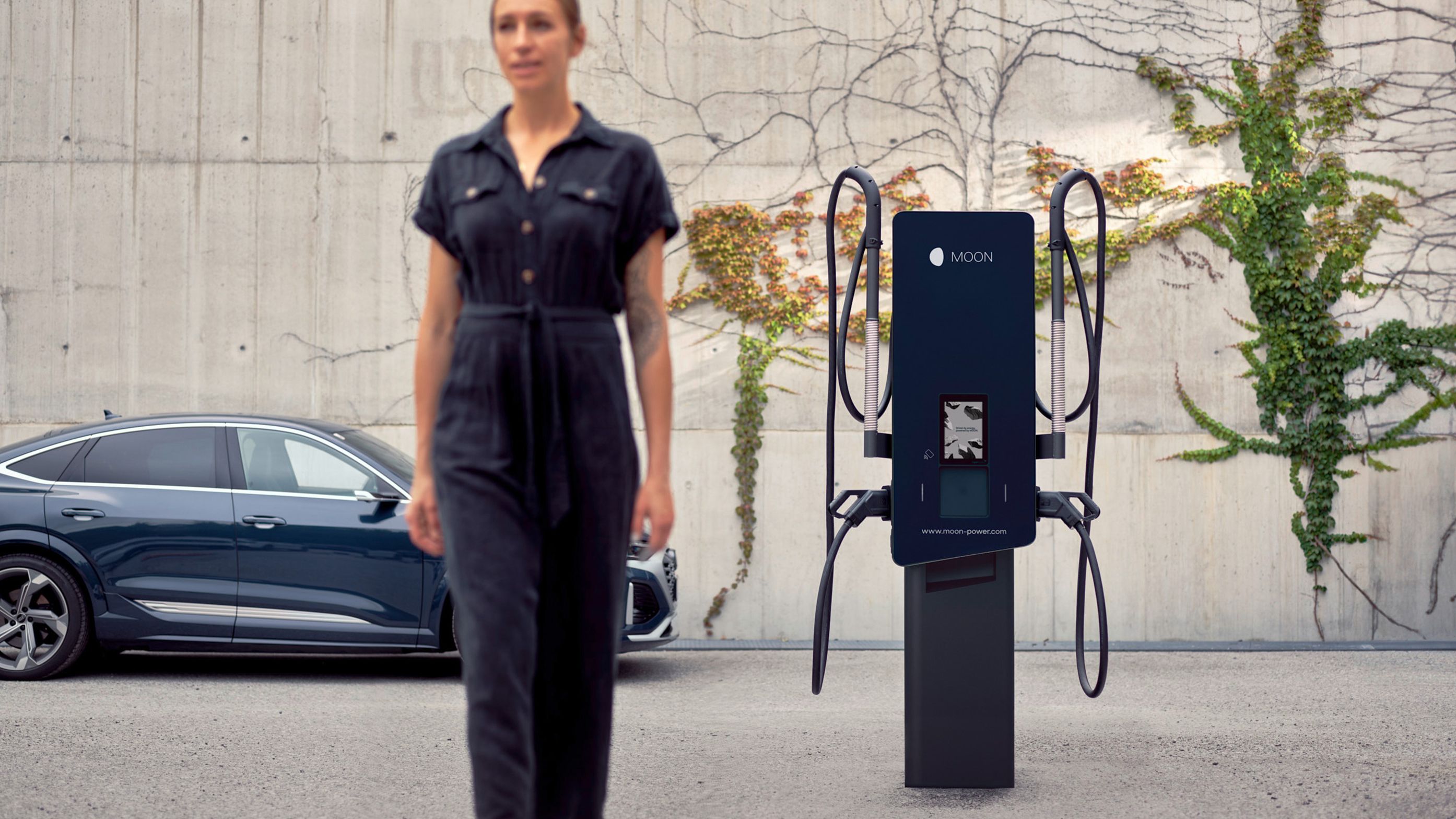 Woman walks in front of a charging station with a car in the background