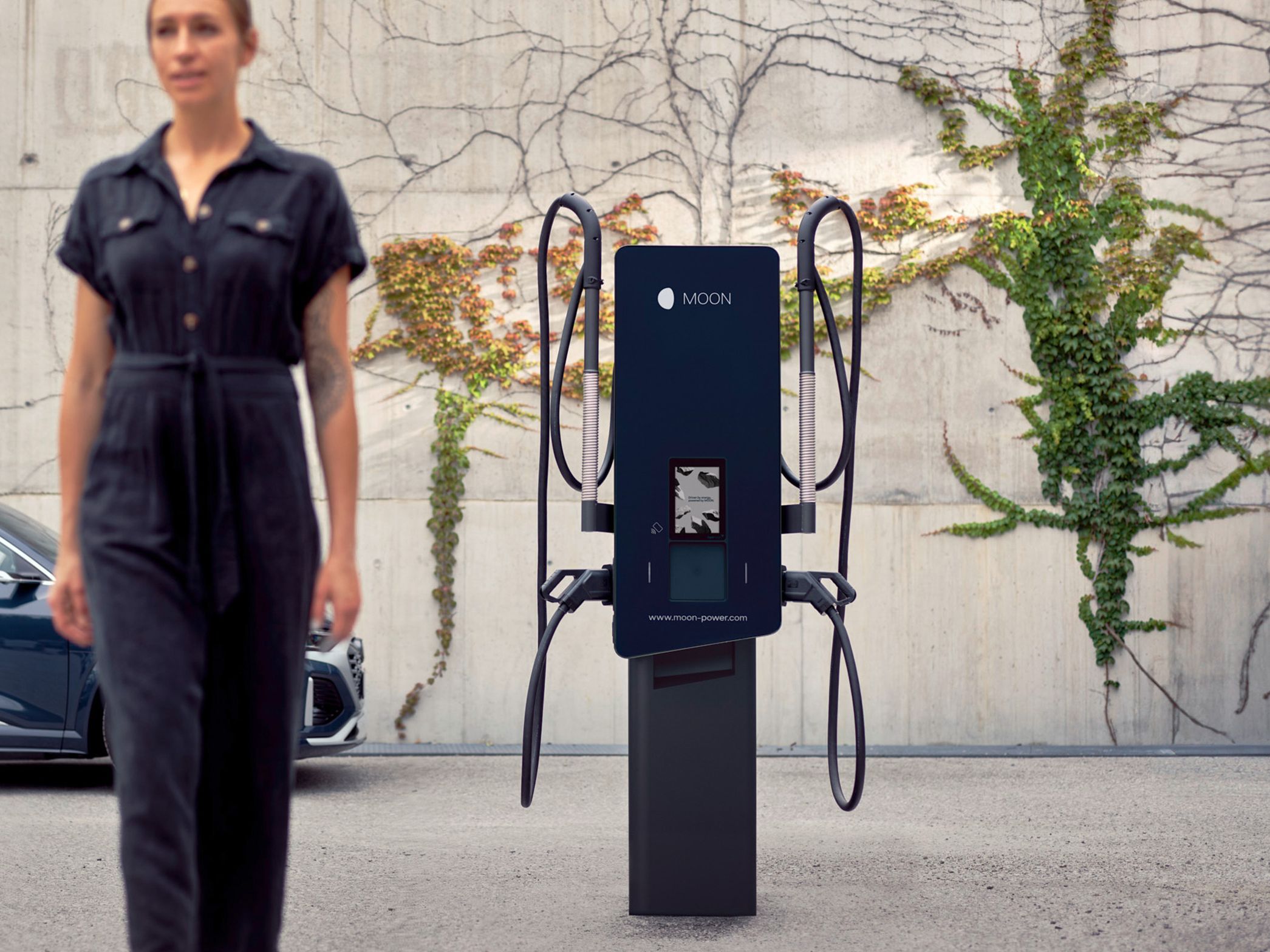 Woman walks in front of a charging station with a car in the background