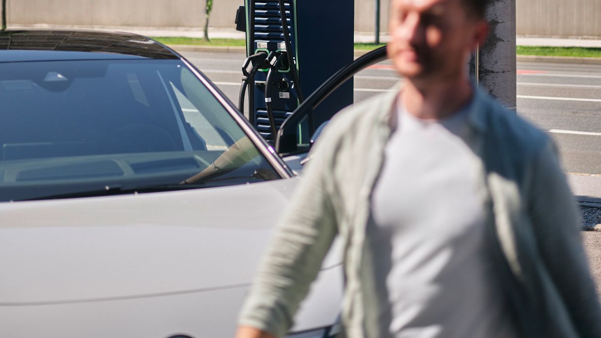 Man walks in front of a car in front of a charging station