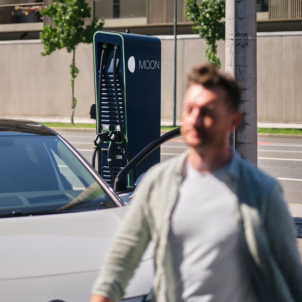 Man walks in front of a car in front of a charging station