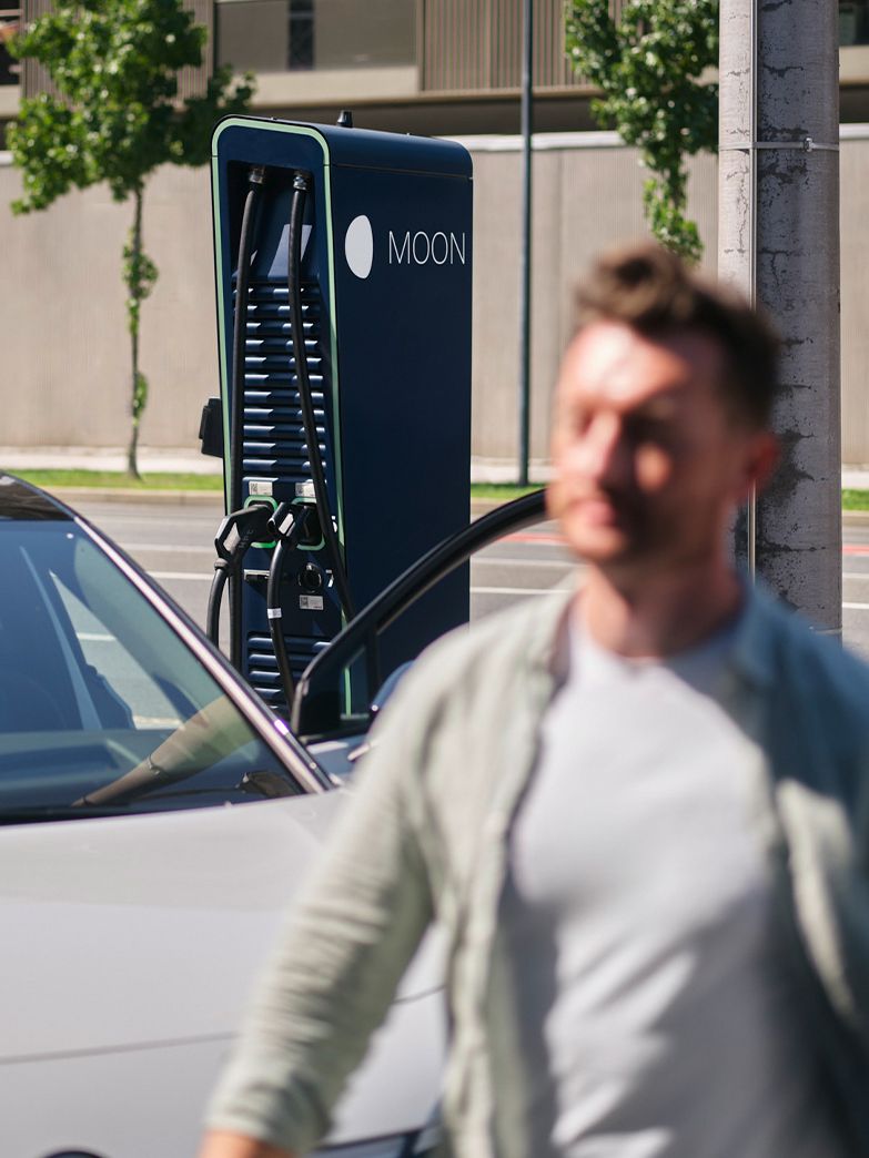 Man walks in front of a car in front of a charging station