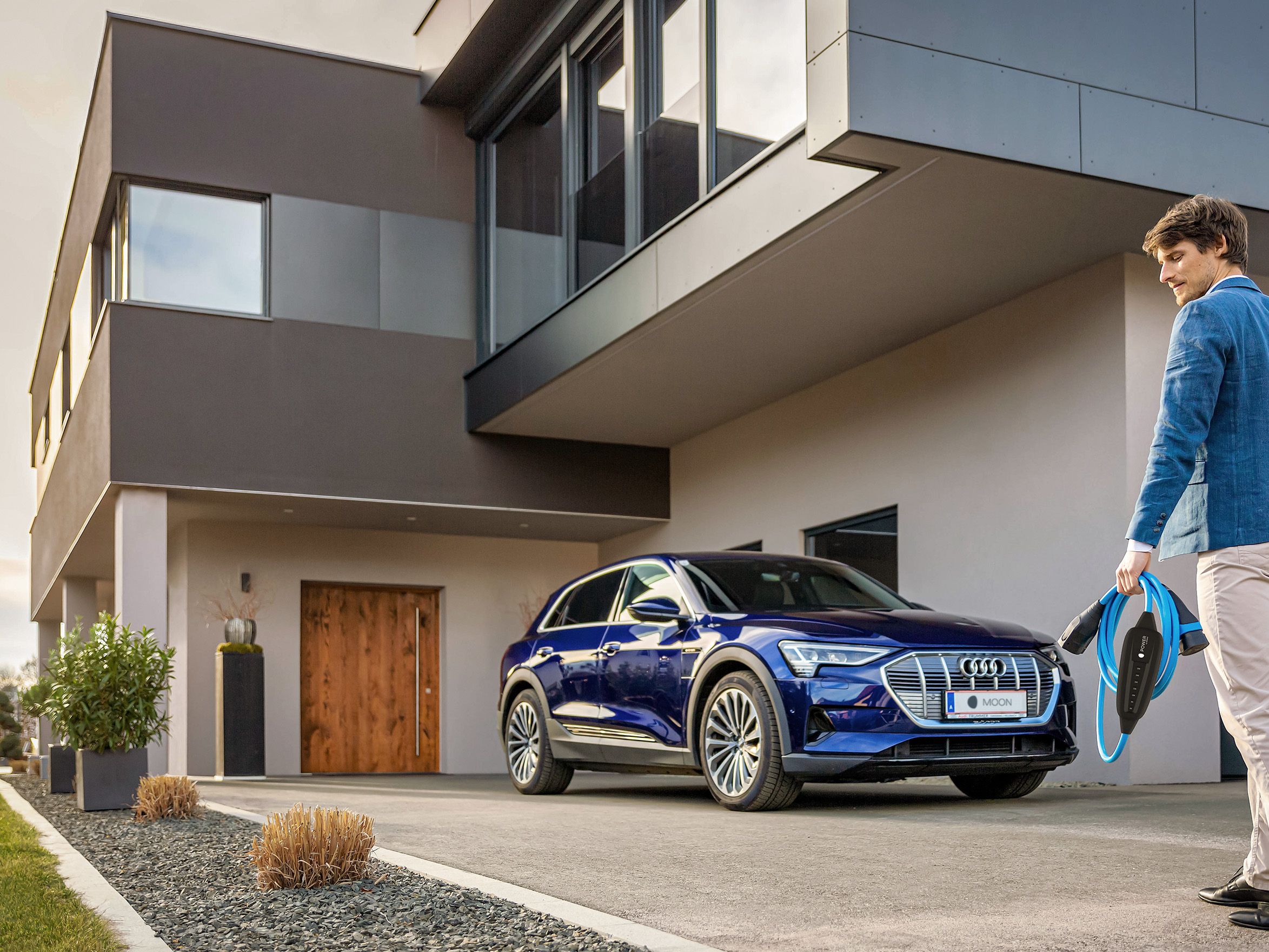 Man walks towards a car near a house with a cable in his hand