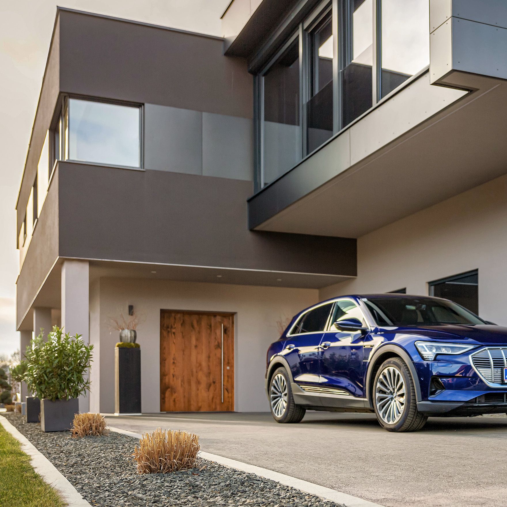 Man walks towards a car near a house with a cable in his hand