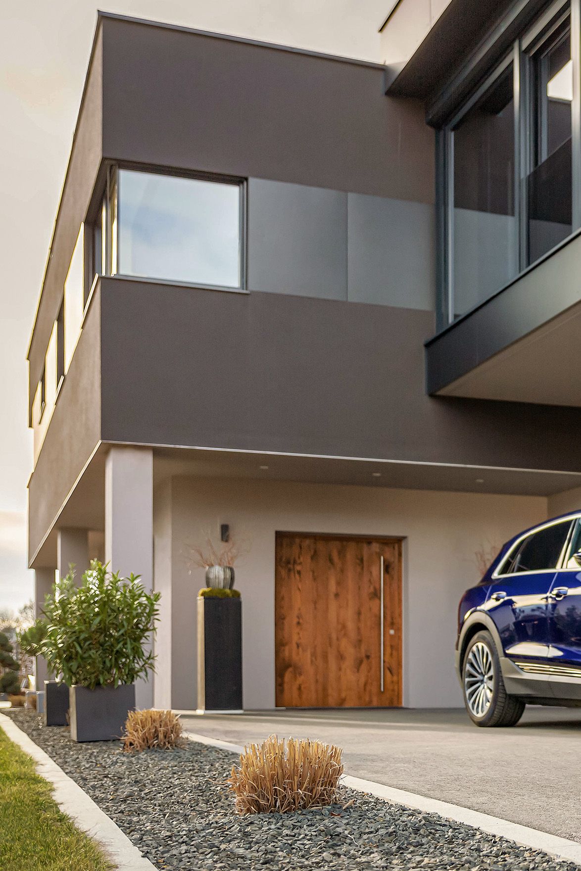 Man walks towards a car near a house with a cable in his hand