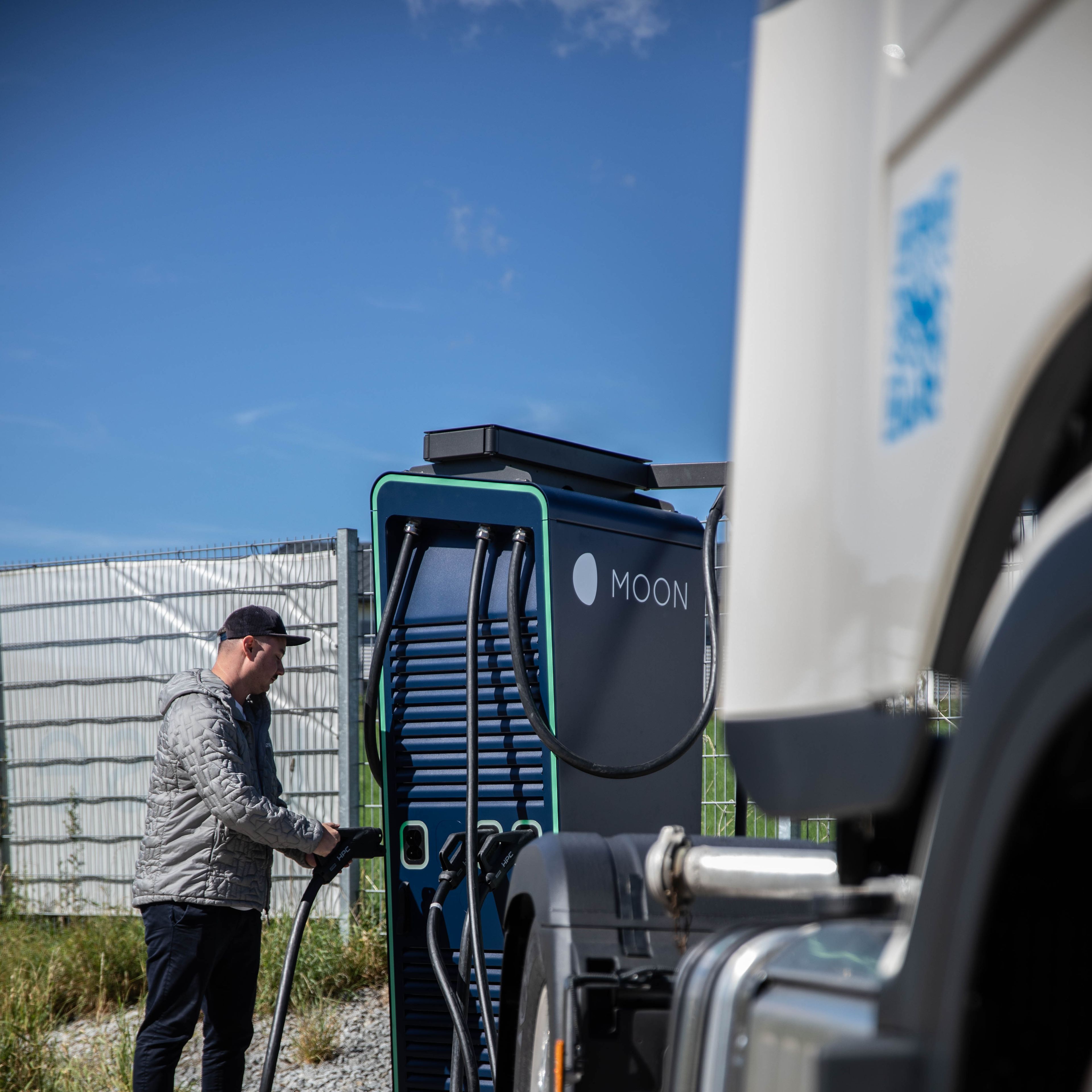 A man holds the plug of a HYC 200-400 fast charging station behind a truck