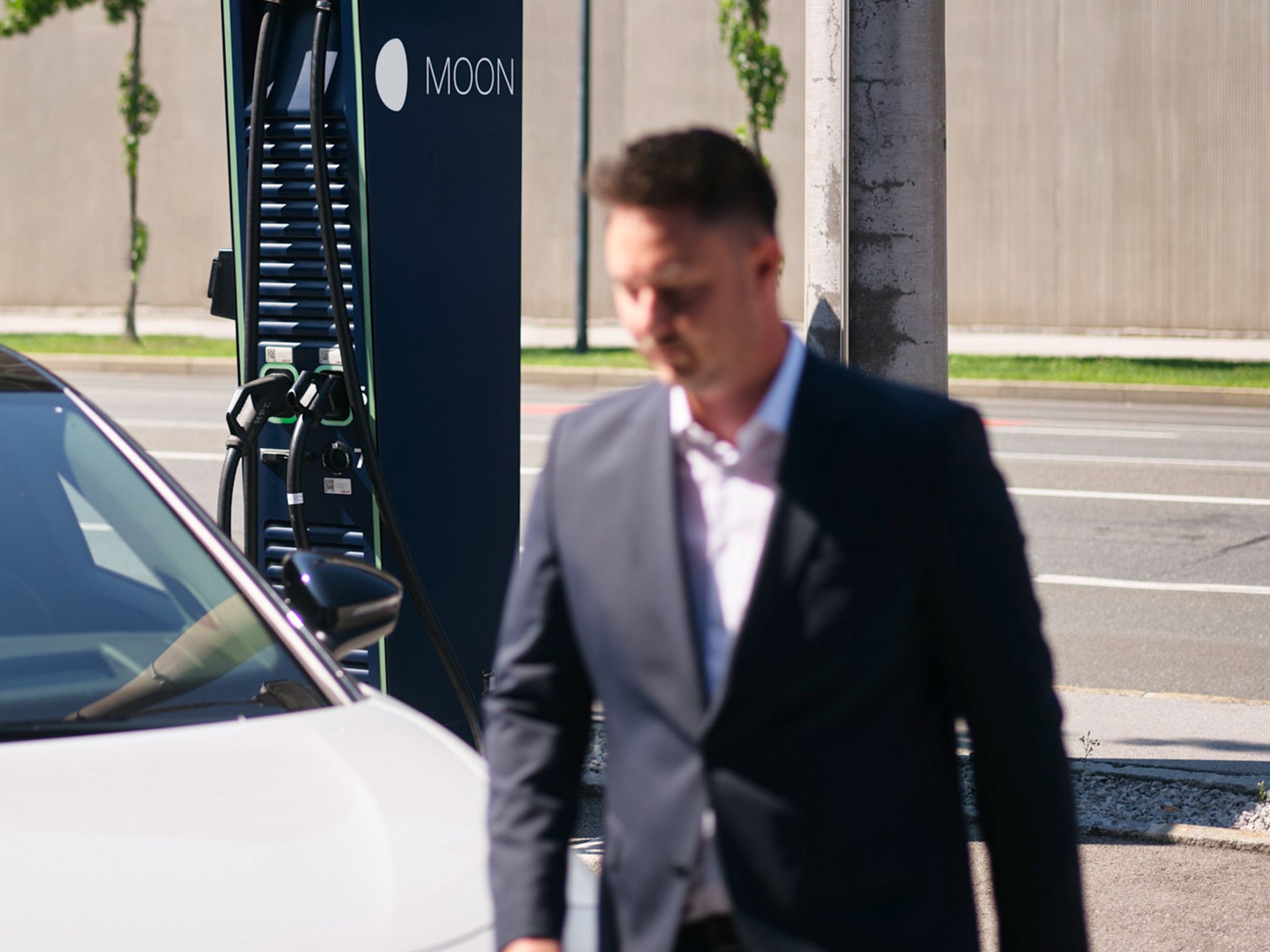 Man walks in front of a car in front of a charging station
