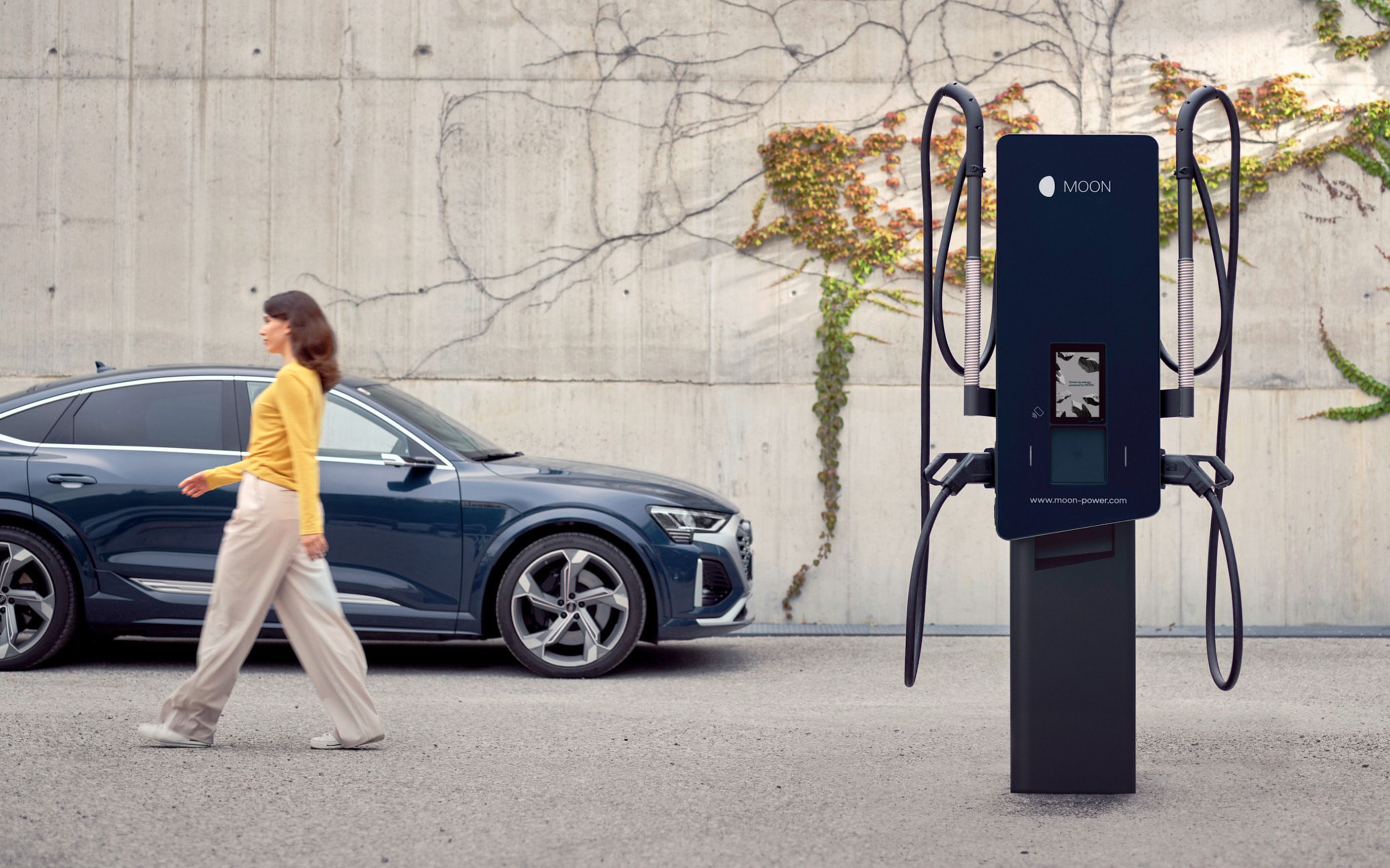 Mulher se afasta de uma estação de recarga passando por um carro