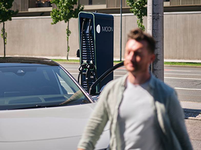 Man walks in front of a car in front of a charging station