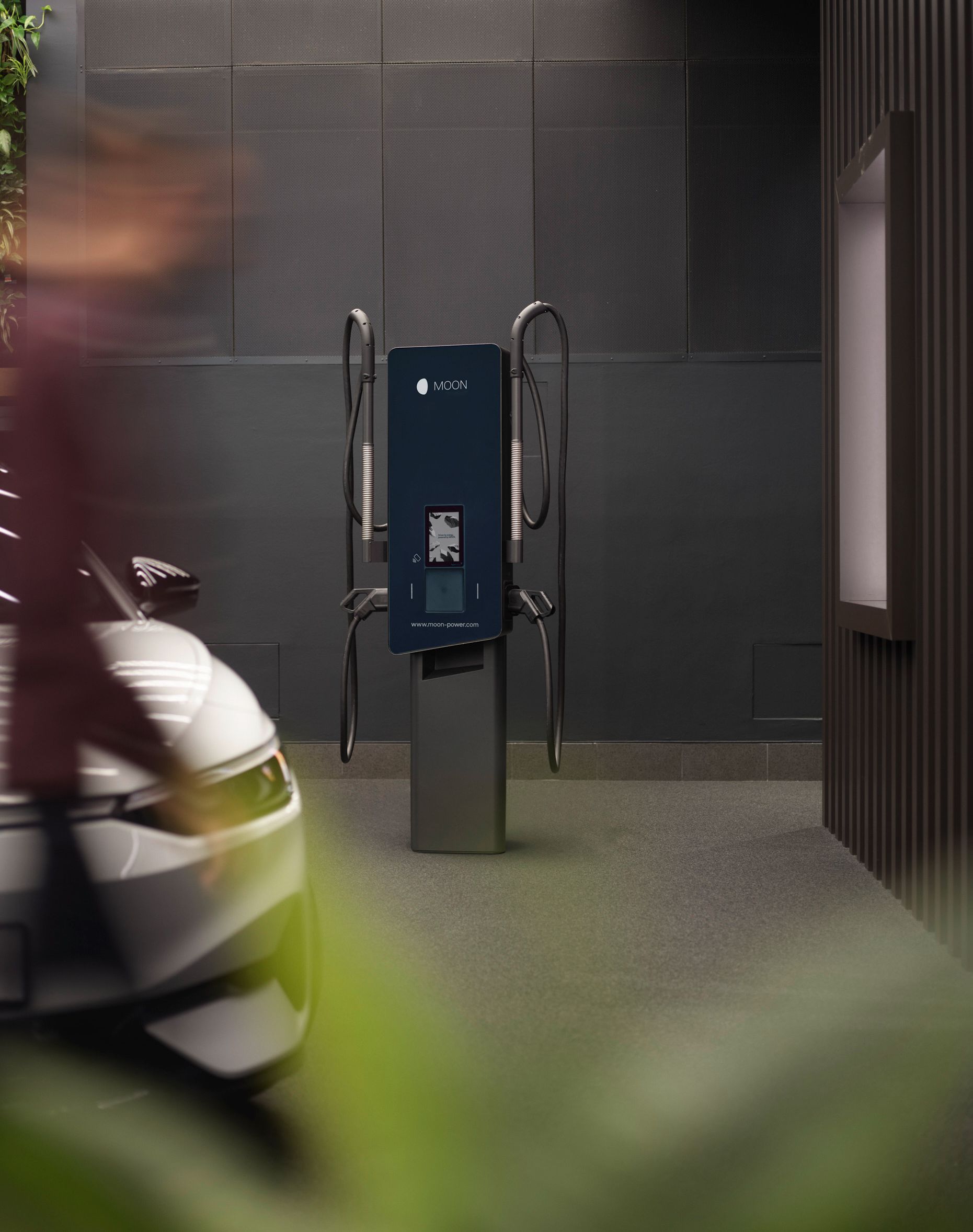 Ladestation vor einer grauen Wand mit Auto im Vordergrund