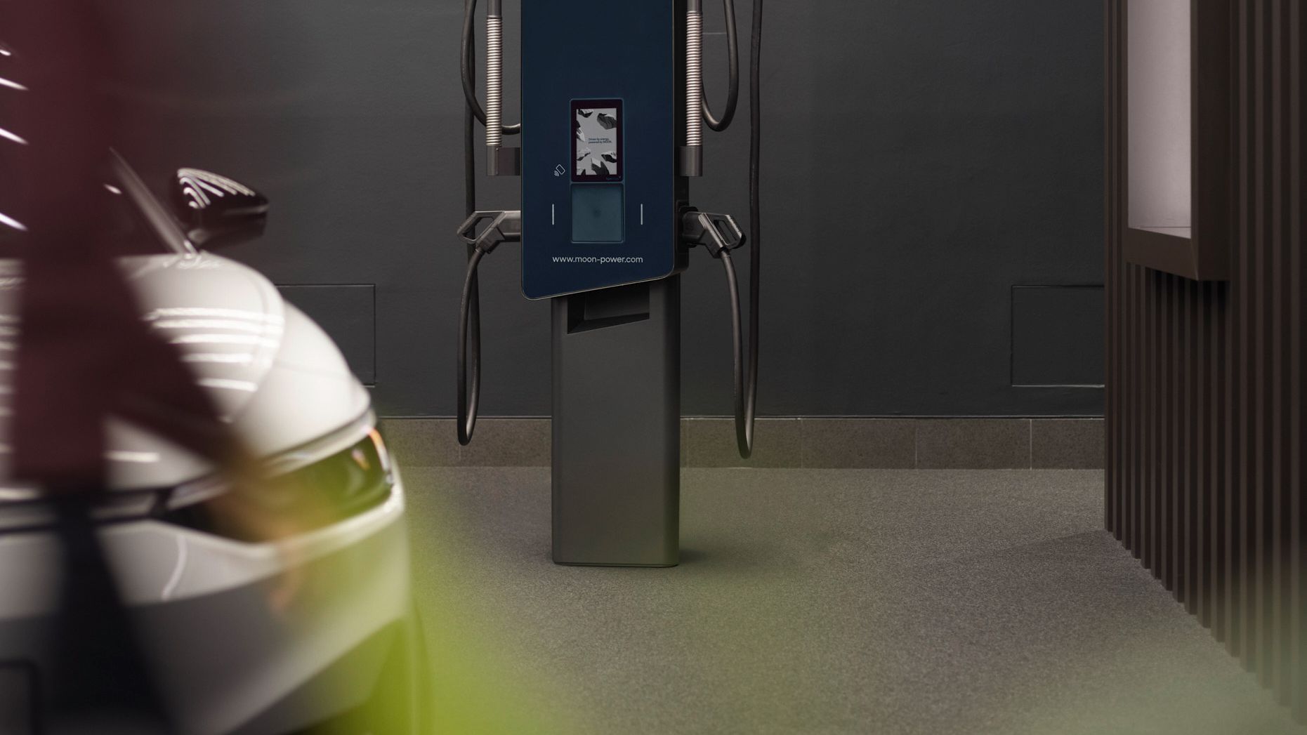Estação de recarga em uma sala com paredes cinza e um carro em primeiro plano